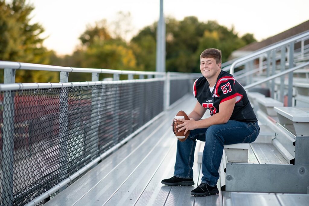 Linganore High School teen boy sitting on bleachers, holding a football.