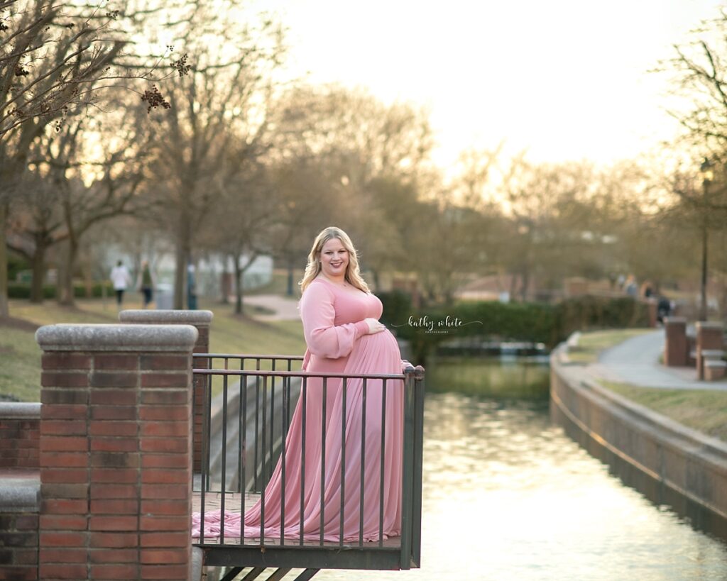 Image of an expecting new parent wearing a pink maternity gown in a park in Maryland.