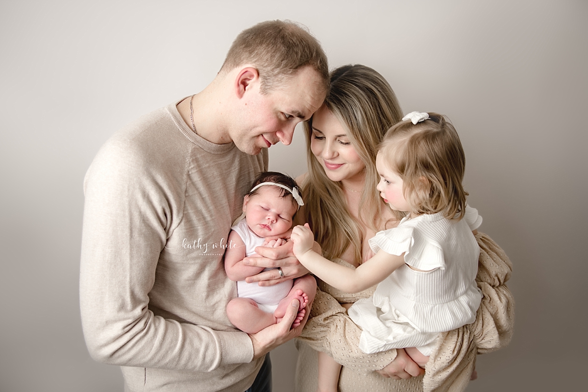Image of a new parents dressed in neutral colors, holding newborn and toddler.