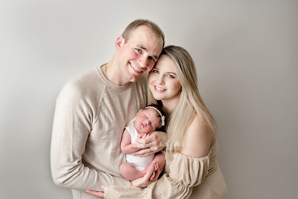 New parents wearing neutral colored clothing, holding their newborn baby girl.