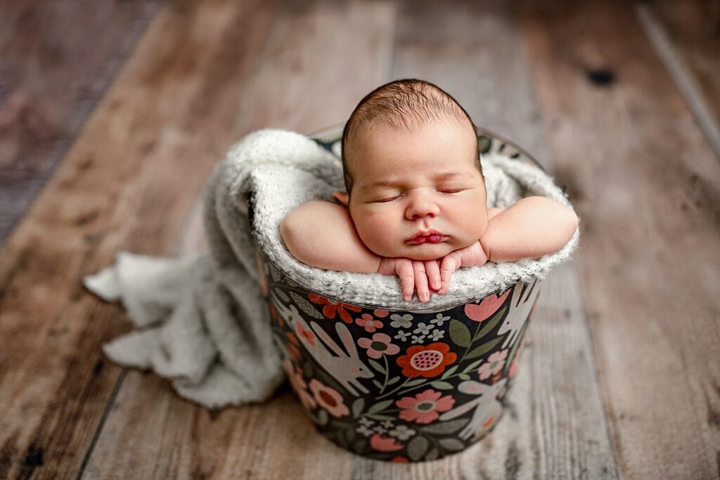 Newborn baby posed inside a bucket that has bunnies and flowers on the outside.