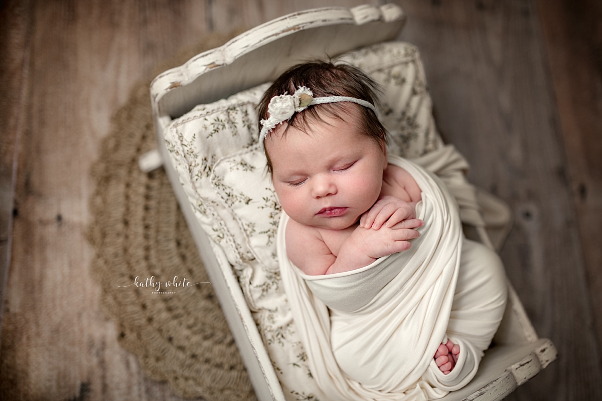 Sleeping newborn baby girl swaddled in a cream colored wrap in a tiny crib.