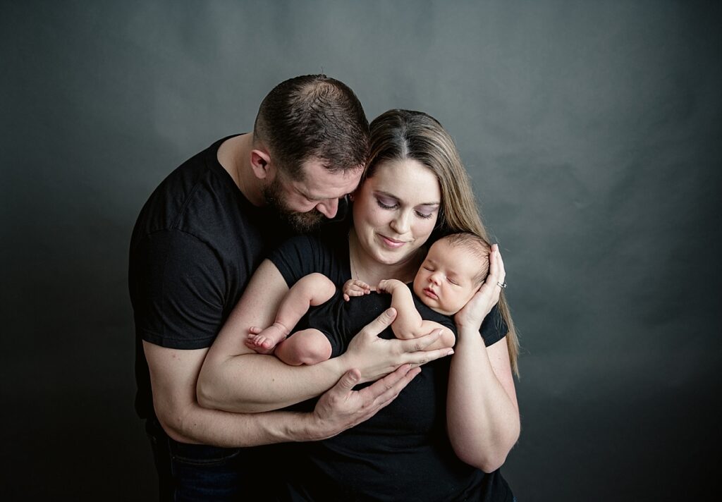 Postpardum mom and dad holding a sleeping newborn baby in a studio.