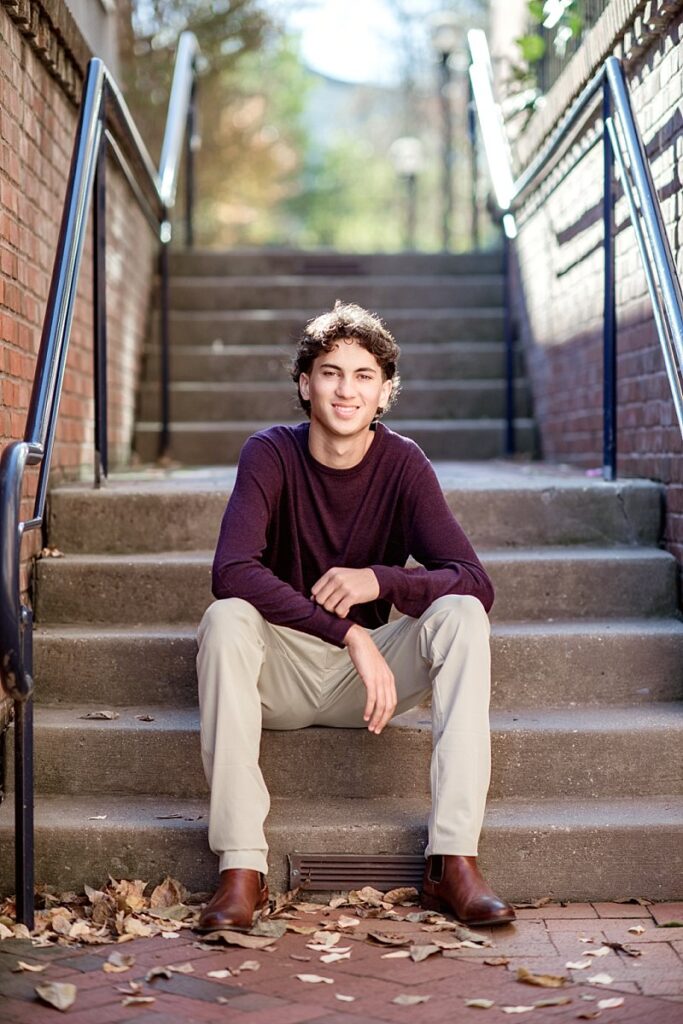 Teen boy sitting on steps in Frederick, Maryland, smiling at the camera.