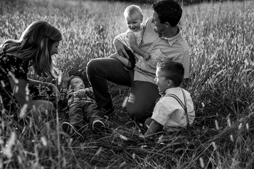 Black and white photo of a family sharing a moment of laughter and playfulness in a field during a photo session.
