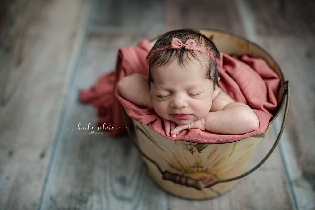 New baby girl posed inside of a bucket with a painted floral design.