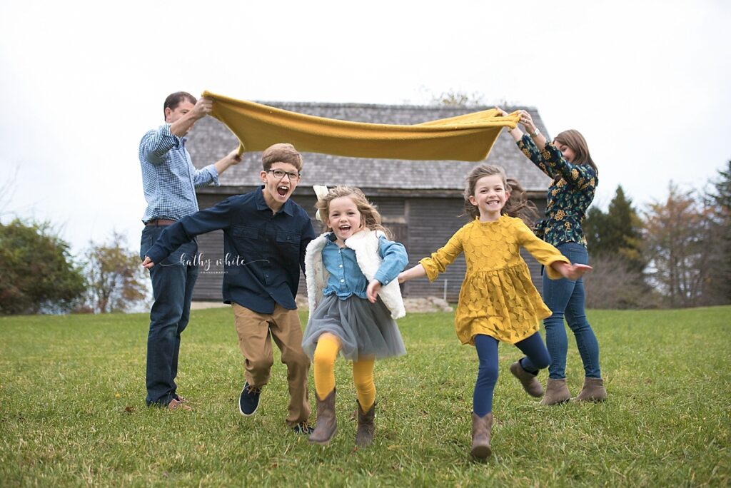 Laughing children running and playing a game with their parents during a photo shoot.
