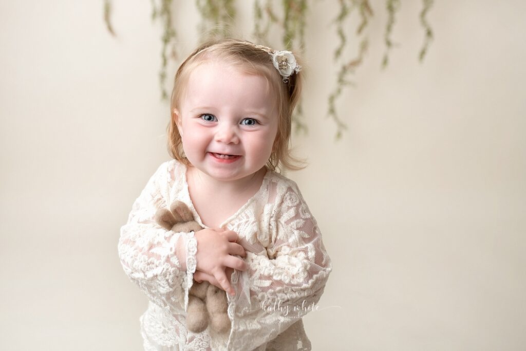 Smiling baby girl, looking at the camera, in a photo studio, holding a stuffed bunny.