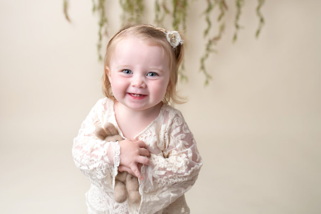 Smiling toddler girl holding bunny stuffed animal in a Frederick County photography studio.